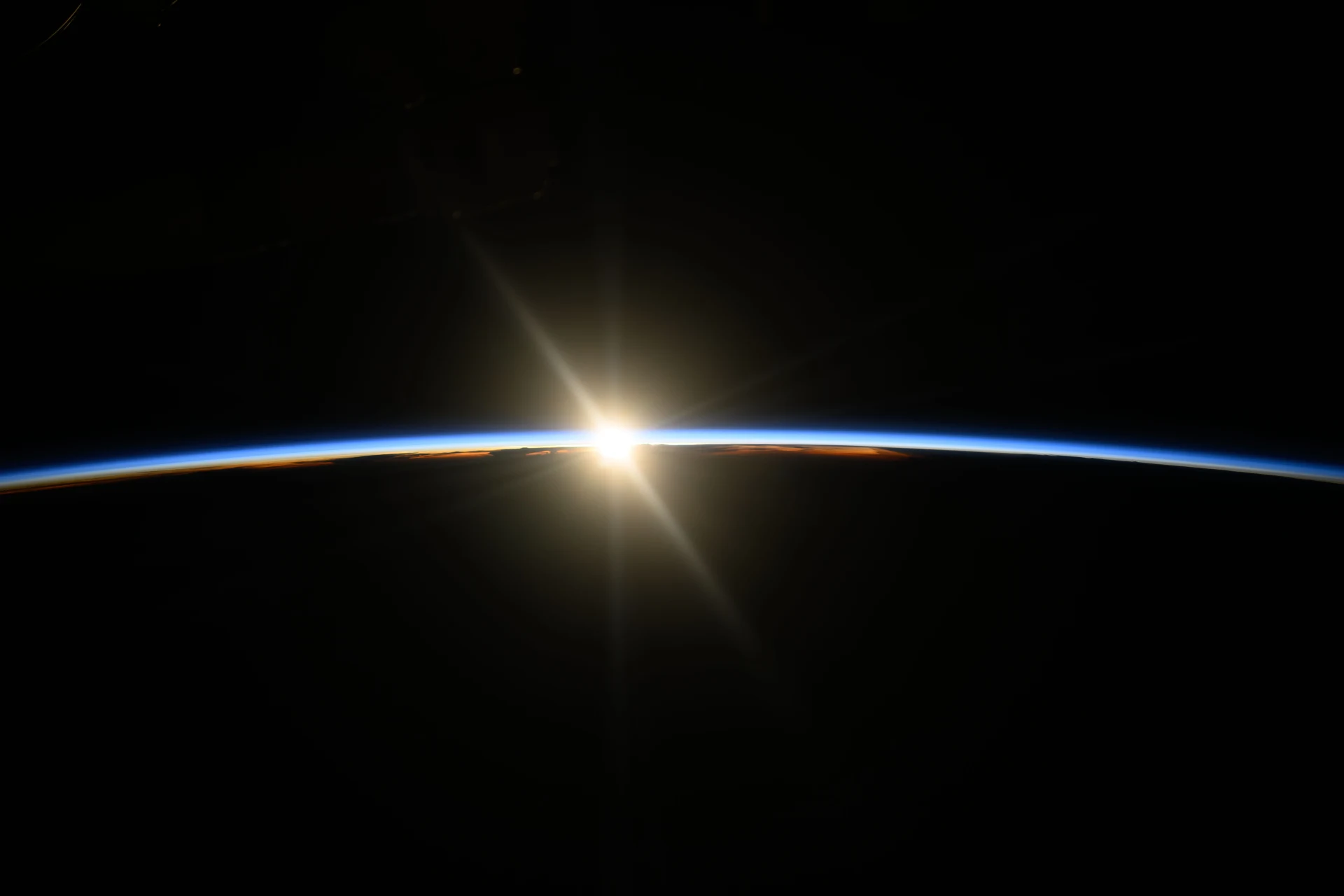 Sunlight rises along Earth’s edge, illuminating a thin blue atmosphere against black space.